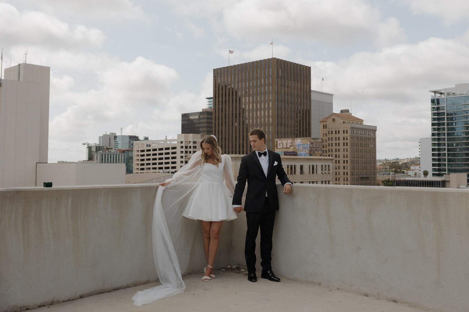 bride in mini dress and groom pose on parking structure after courthouse wedding